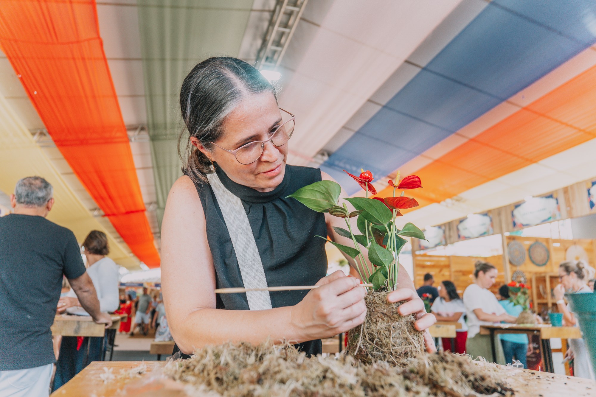 Participante trabalha no preparo de uma planta com flores vermelhas durante a Expo Flores.